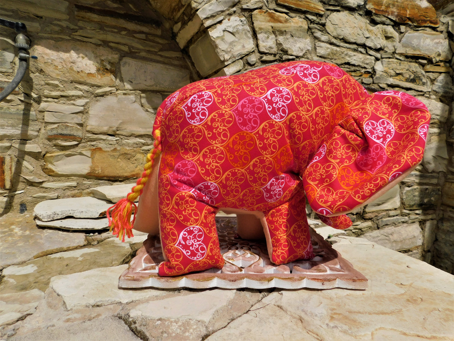 Decorative elephant figurine with red and pink patterns against a stone wall.
