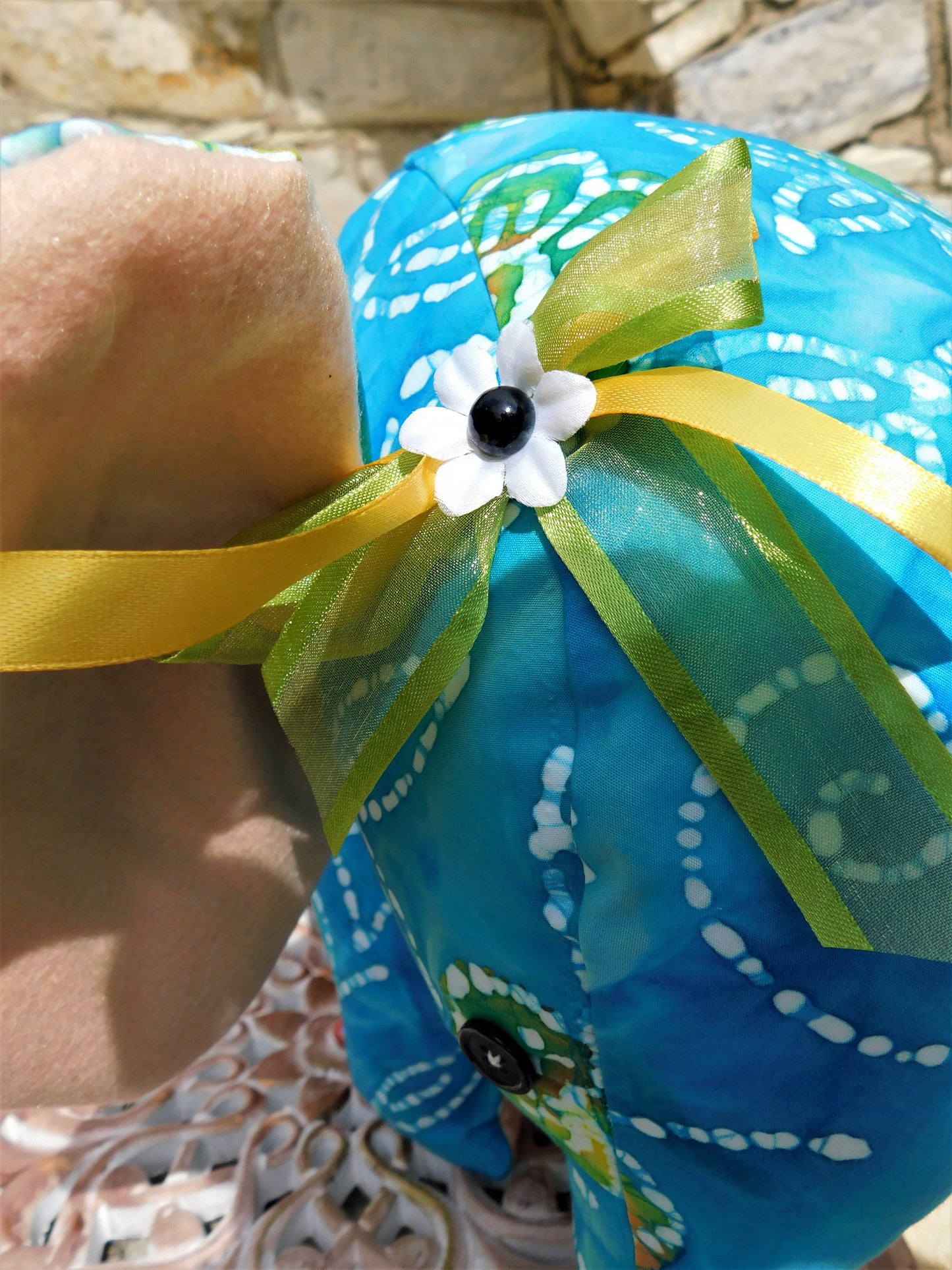 Blue decorative item with yellow ribbon and white flower against a stone wall background