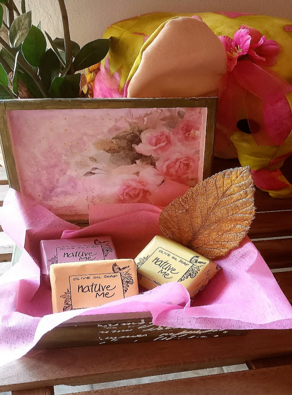 Gift set with soaps and a leaf on pink tissue paper, framed floral picture in the background.