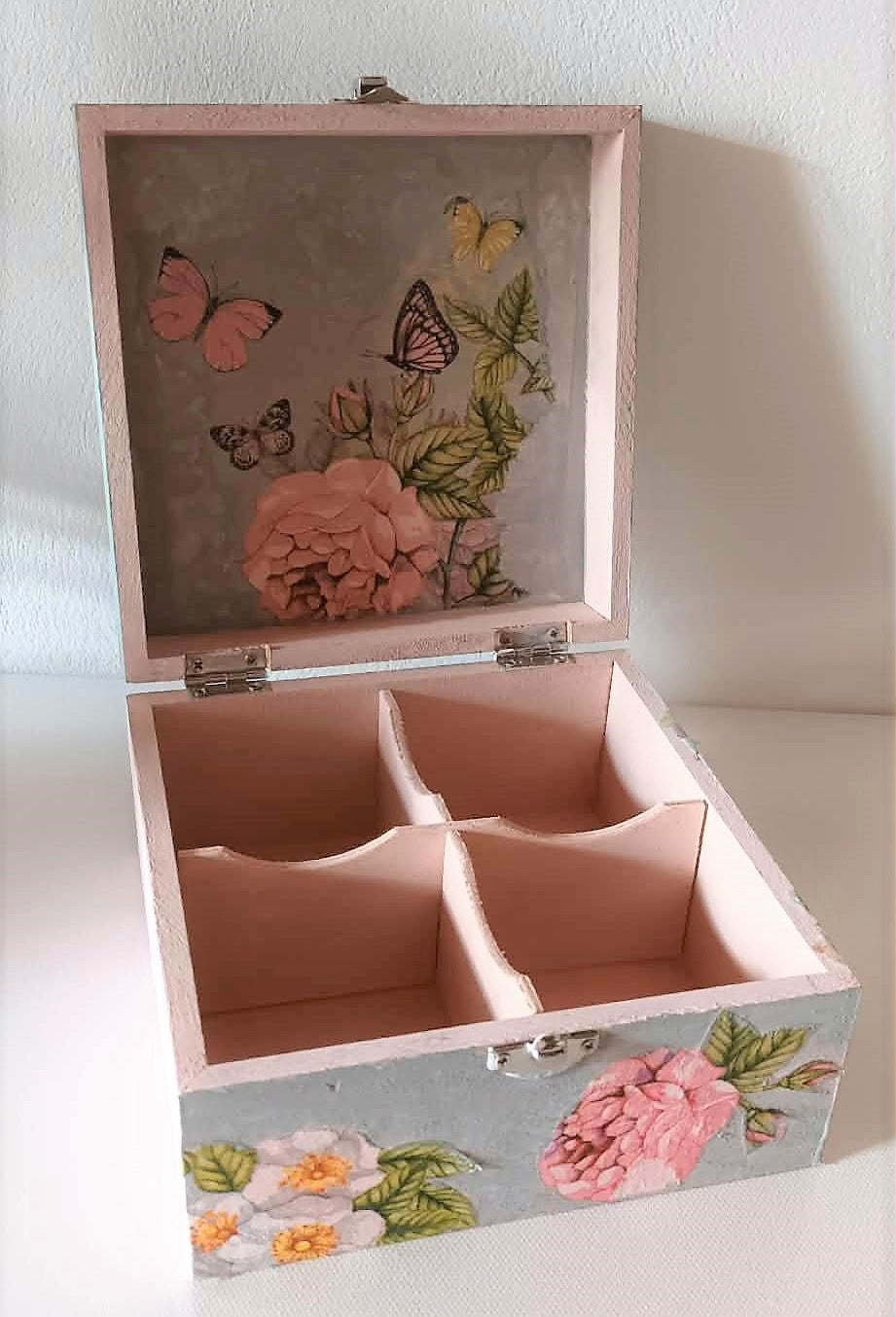 Hand crafted wooden box with floral and butterfly design on a soft pink background with four compartments