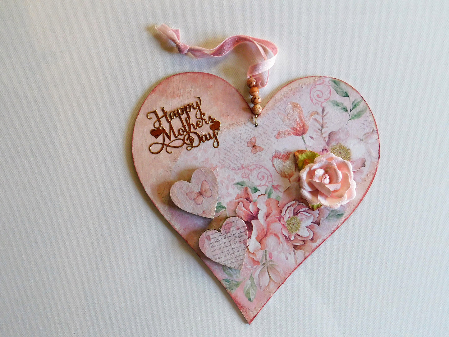 Heart-shaped Mother's Day wooden card with floral designs and a pink ribbon on a light background