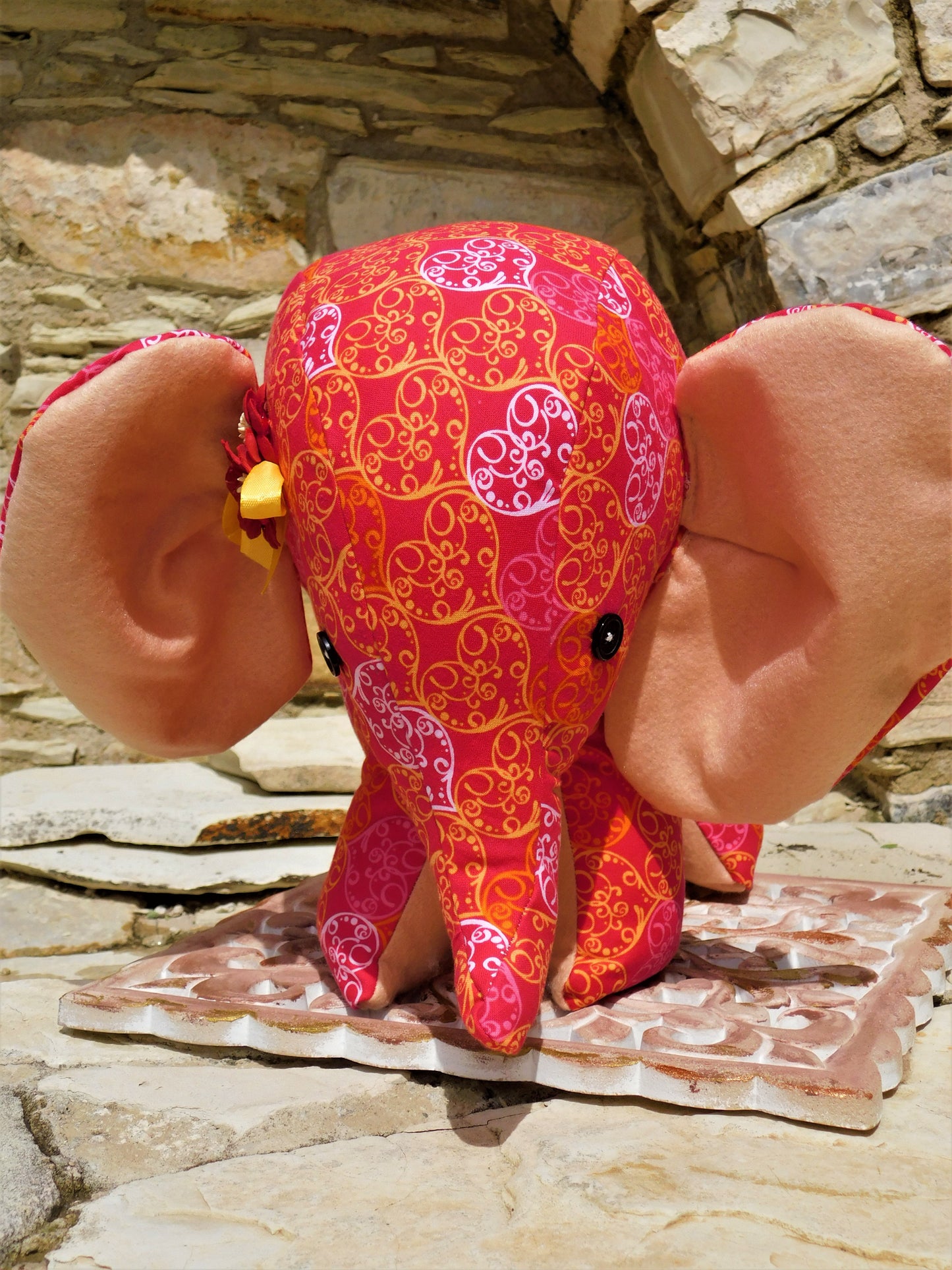 Decorative elephant plush toy with pink and orange patterns on a stone surface.