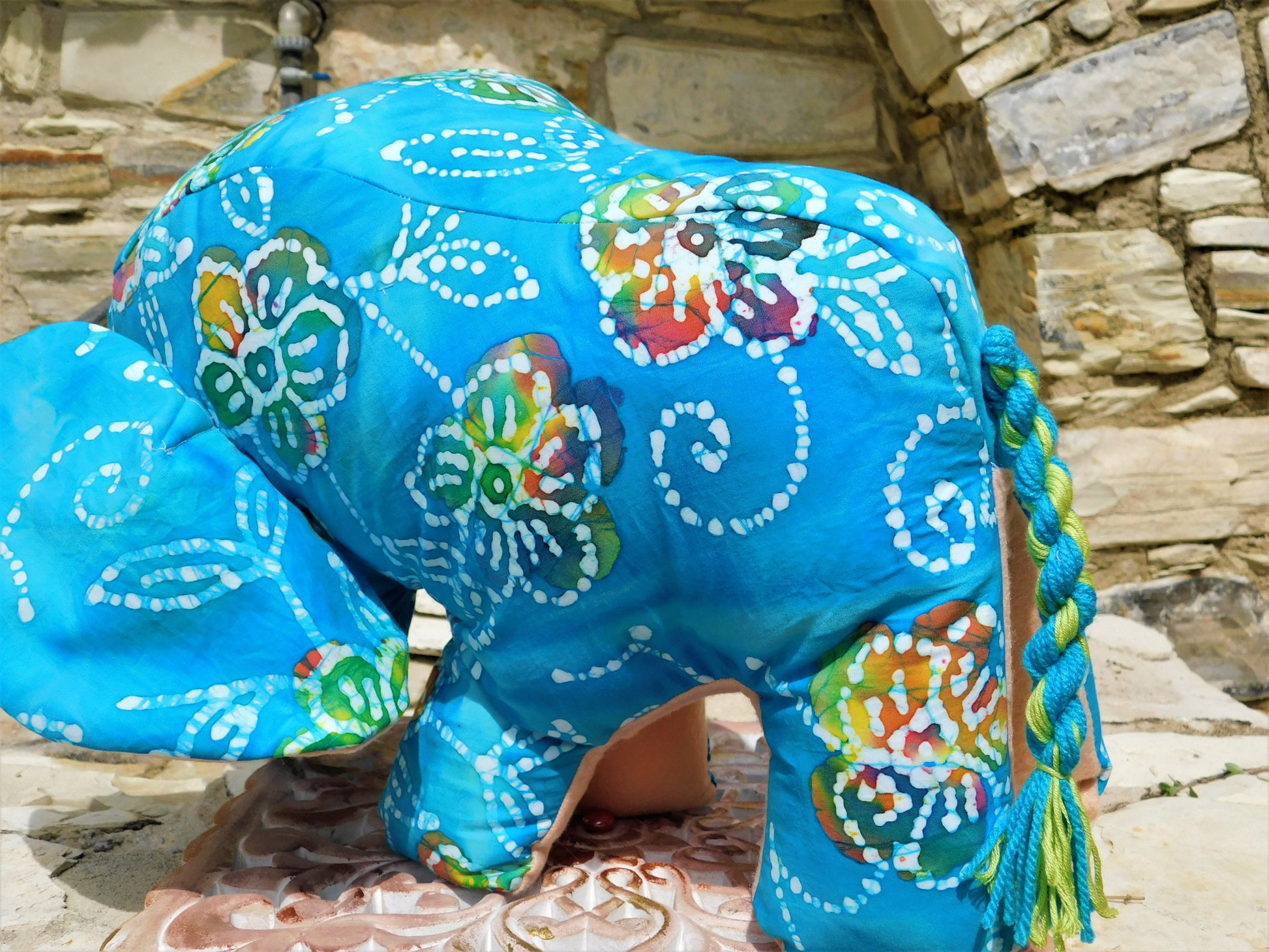 Decorative elephant with blue patterned design against a stone wall background