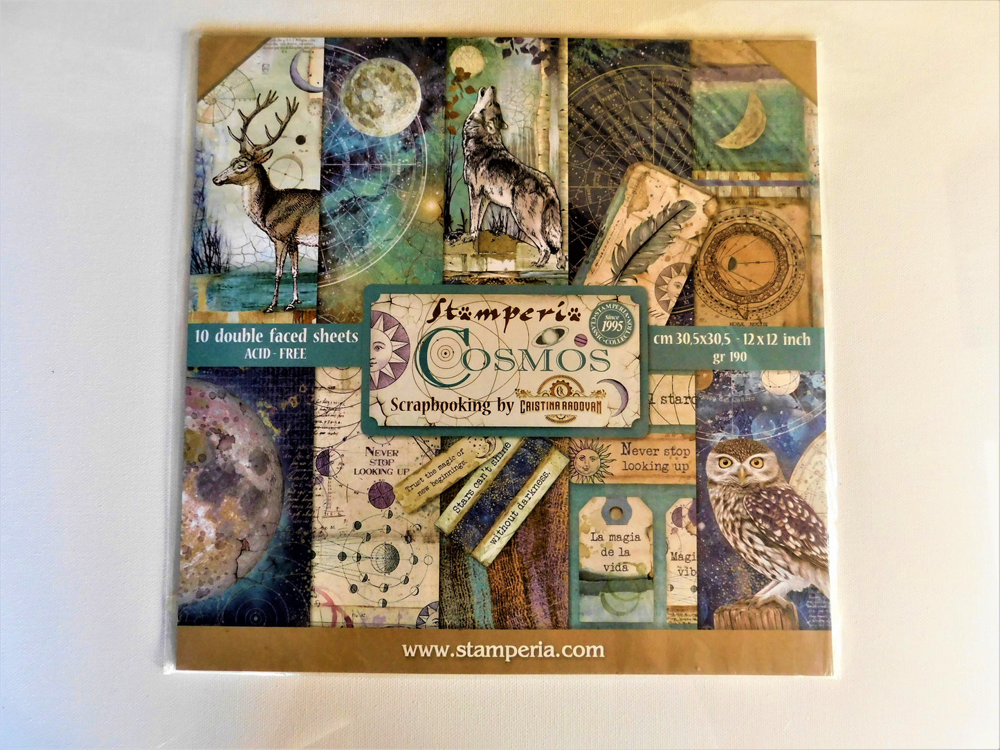 A square scrapbooking paper sheet set titled 'Stamperia Cosmos' with a collage of vintage-style illustrated panels, including a deer, wolf, owl, moon, compass, and script elements.