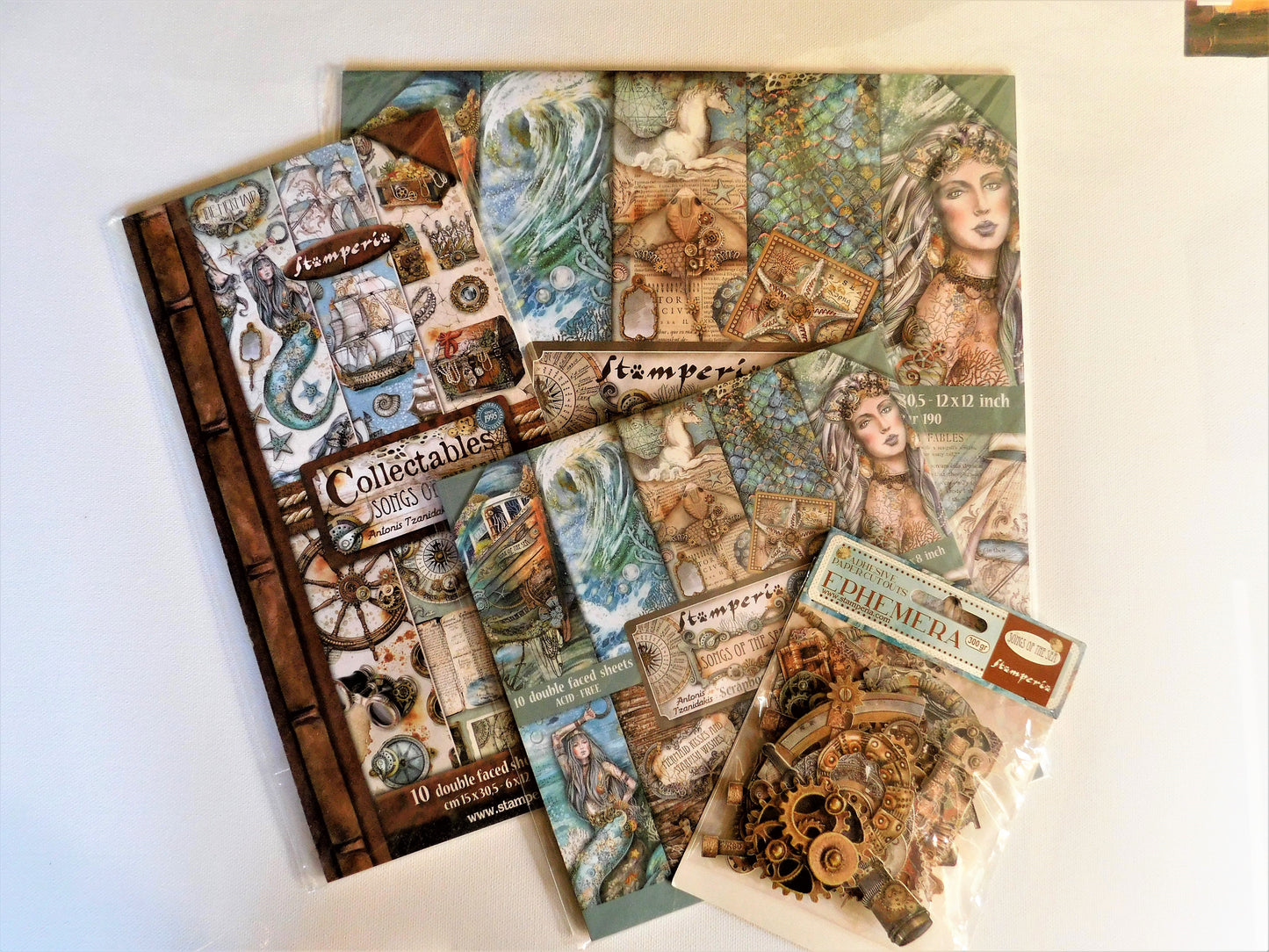 A collection of vintage-themed scrapbooking papers and embellishments from  Stamperia, designed by Antonis Tzanidakis.  The designs feature a mermaid, an antique, steampunk aesthetic with sepia tones, gears, clocks, and illustrations of sea elements